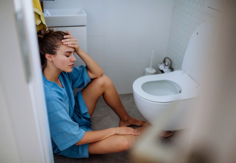 Frau sitzt vor einer Toilette auf dem Boden