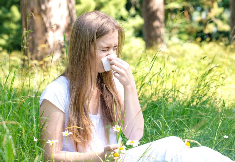 Junge Frau mit Pollenallergie sitzt auf einer Wiese
