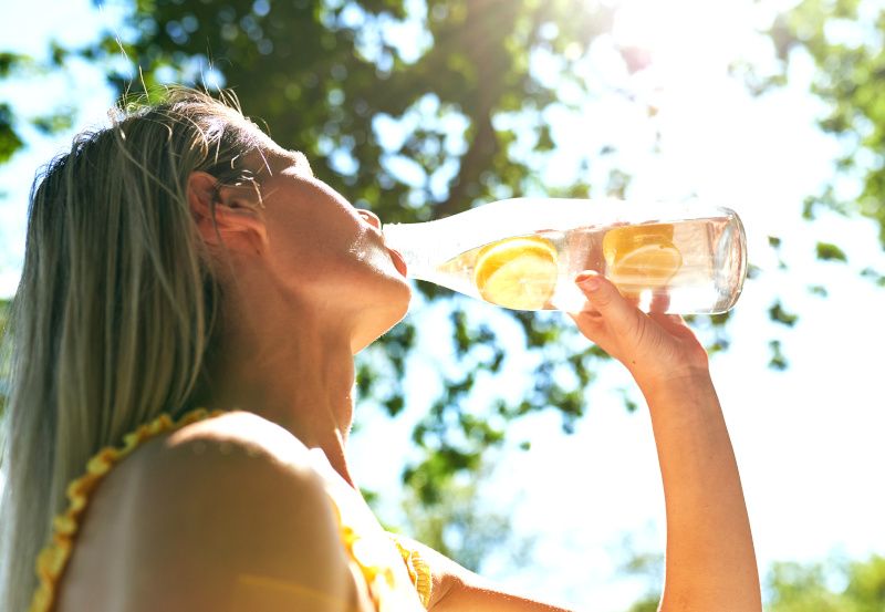 Frau trinkt in der Sonne Wasser mit Zitronenscheiben