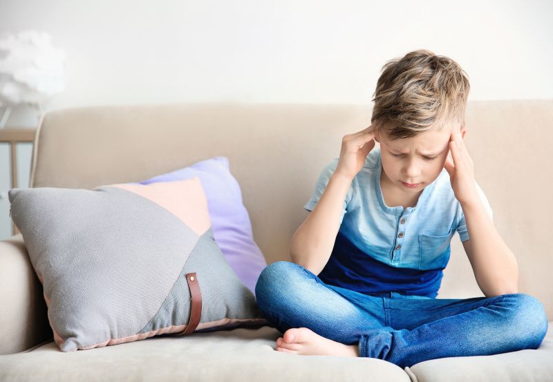 Bub mit Kopfschmerzen sitzt auf einer Couch