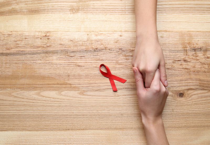 Zwei Hände halten sich, rote AIDS-Schleife