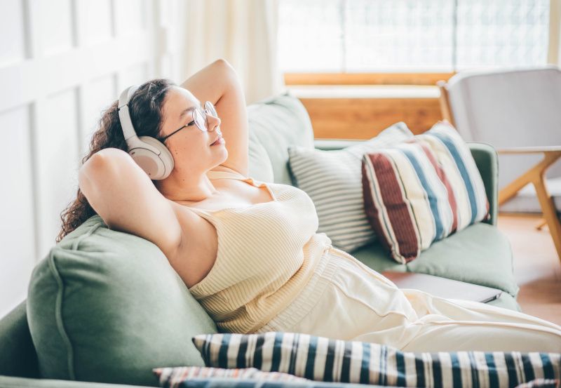 Junge Frau sitzt entspannt auf einer Couch und hört Musik