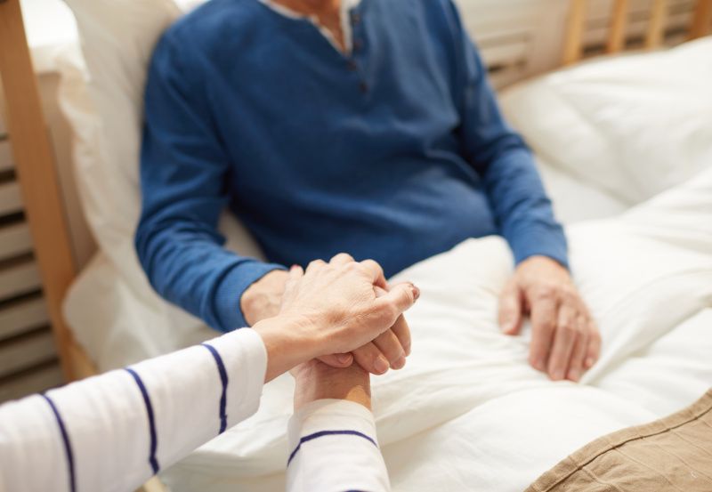 Mann liegt im Bett und Frau hält seine Hand